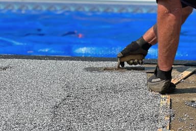Close-up of rubber aggregate being hand-troweled onto pool deck