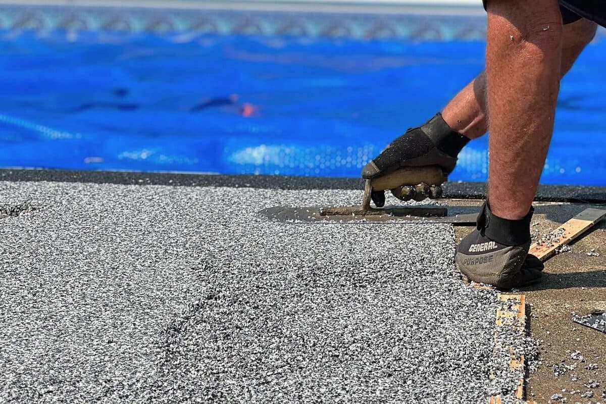 Installer hand-troweling rubber aggregate onto a pool deck surface — ProShield Epoxy installation in progress